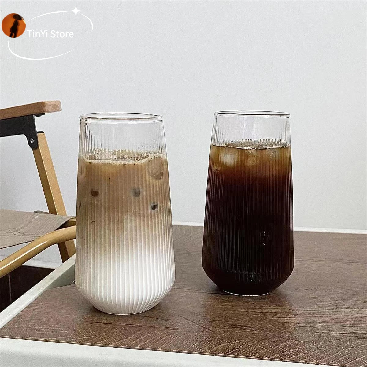 Two clear glass coffee cups on a wooden table, one with a light colored drink and one with a dark colored drink, showcasing the heat-resistant feature.