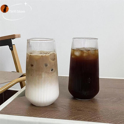 Two clear glass coffee cups on a wooden table, one with a light colored drink and one with a dark colored drink, showcasing the heat-resistant feature.