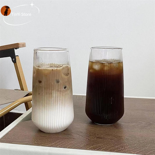 Two clear glass coffee cups on a wooden table, one with a light colored drink and one with a dark colored drink, showcasing the heat-resistant feature.
